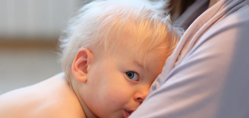 Mother breastfeeding her blonde one year old baby boy toddler. Indoor portrait